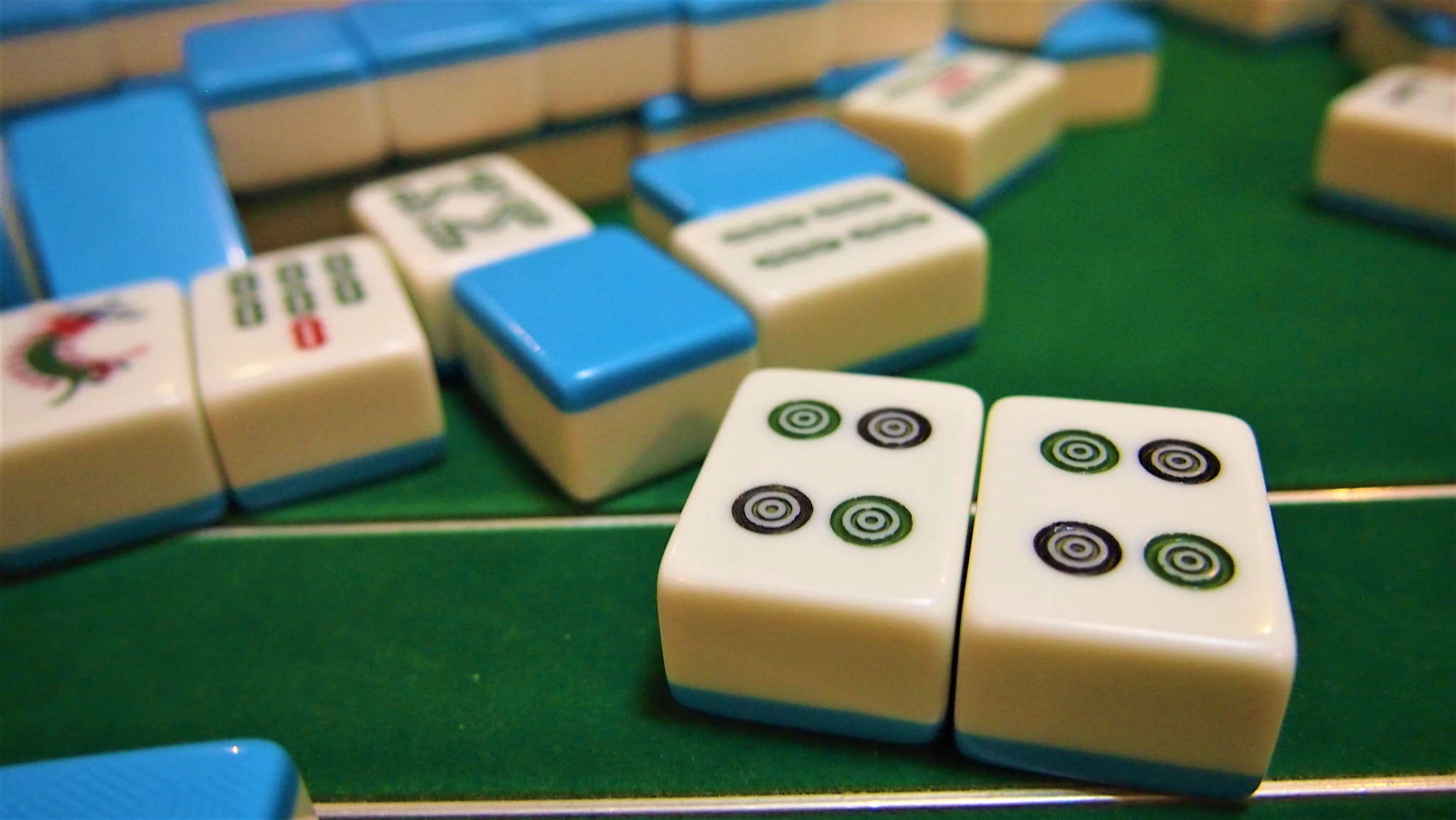 Two four-circle Mahjong tiles in front of blue-backed tiles on a green table.